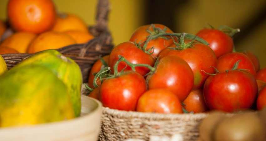 Tomatoes in a basket next to fruit.