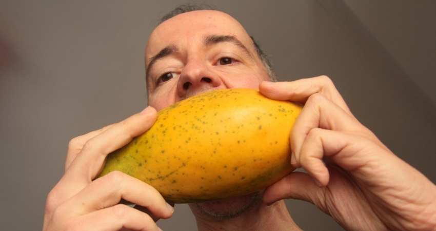 A man biting a mango.