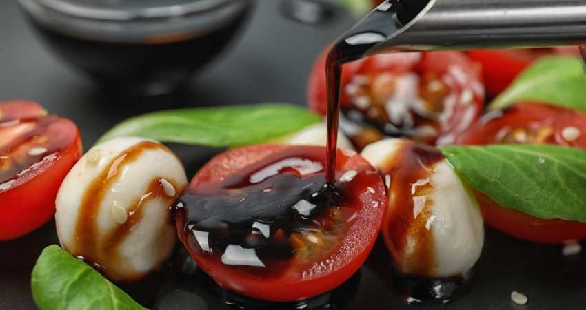 Balsamic vinegar being poured onto tomato and a salad.