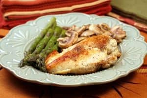 chicken breast dinner on a plate with asparagus and mushrooms